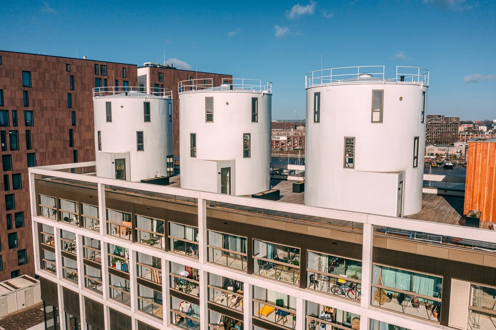 Architectonische vogelvlucht van de iconische witte wijnsilo’s op Cruquius, met moderne uitbouwen, dakterras en strakke beplanting onder een heldere blauwe lucht.