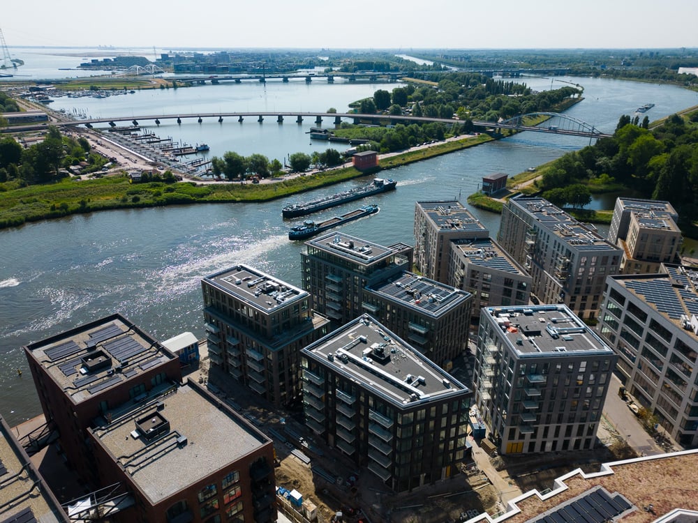 Luchtfoto van nieuwbouwappartementen in Cruquius, Amsterdam-Oost, met uitzicht op het Amsterdam-Rijnkanaal, passerende binnenvaartschepen en meerdere bruggen in het landschap.