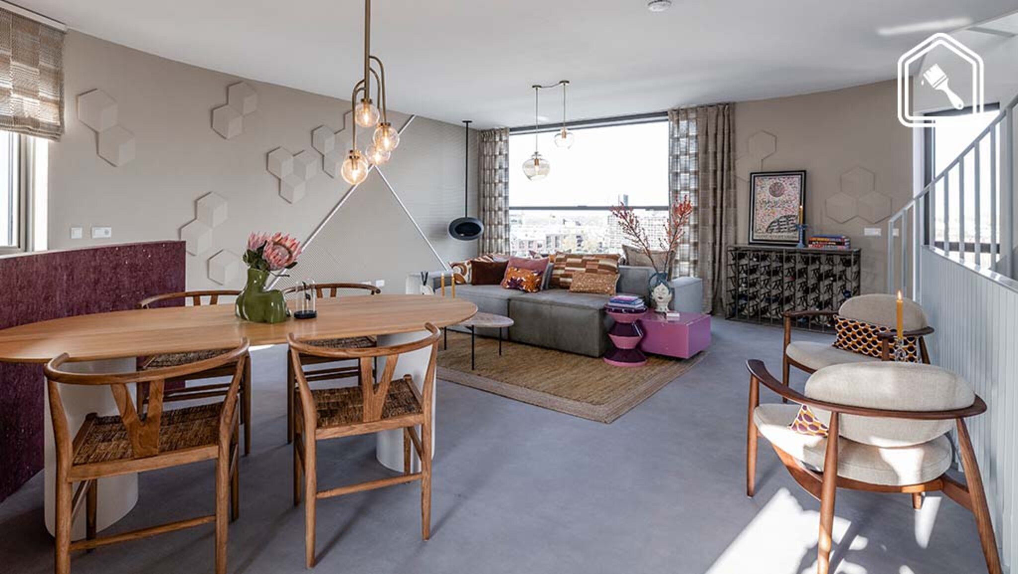 Open woonruimte met ovale houten eettafel, retro eetkamerstoelen, zachte wandstructuren en een gezellige zithoek met aardetinten, designverlichting en uitzicht over de stad.
