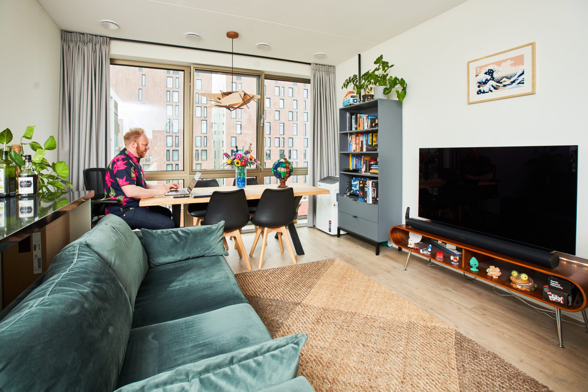 Rob Thijs zit geconcentreerd achter zijn laptop aan een houten eettafel in een licht en modern appartement in Cruquius, omringd door boeken, planten en designaccenten.