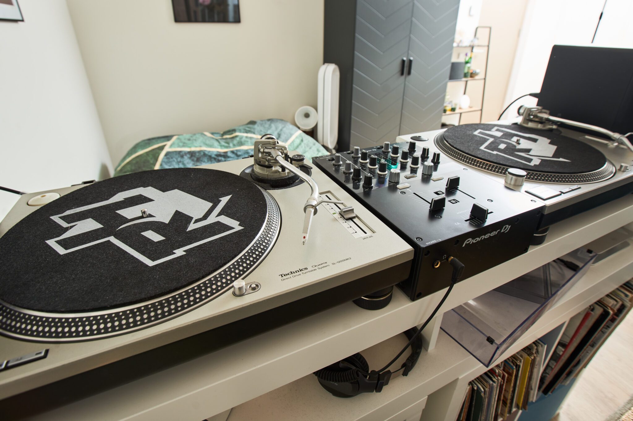 Nabijbeeld van Robs draaitafels en mengpaneel, met op de achtergrond een bed en een kast. Onder de DJ-set zijn diverse vinylplaten zichtbaar opgeborgen.