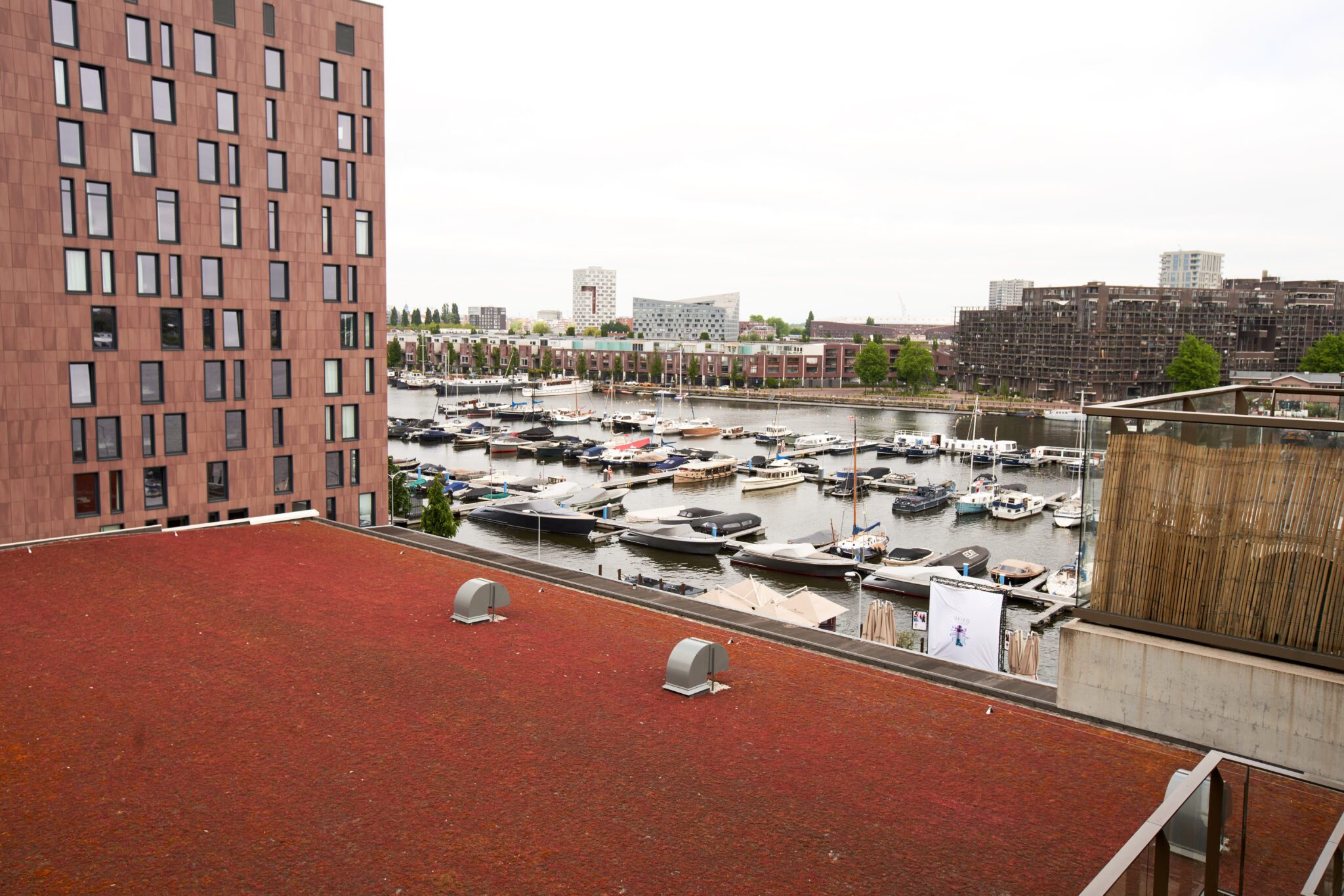 Uitzicht vanuit de studio van Rob op de Entrepothaven in Cruquius, met tientallen boten aangemeerd en moderne gebouwen op de achtergrond.