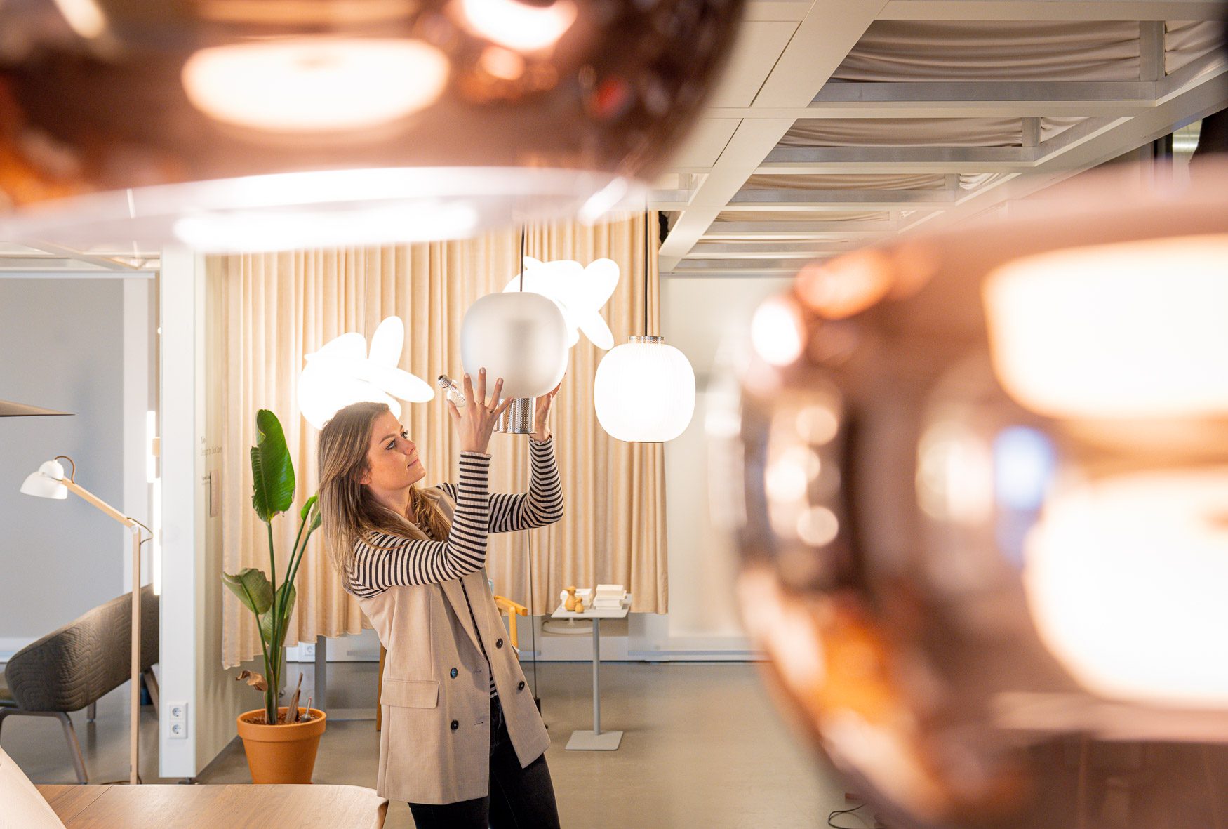 Vrouw stelt een designlamp af in een showroom vol moderne verlichting in warme tinten.